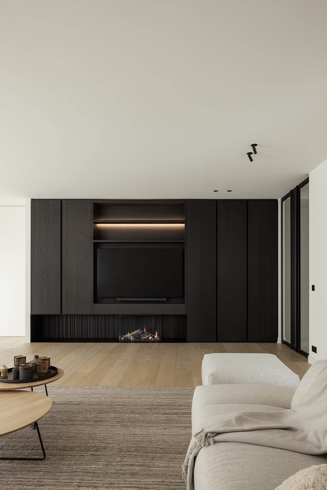 Ruime woonkamer met een tv-kast in donkere houttinten en een subtiele ingebouwde haard voor een strakke, moderne uitstraling.
